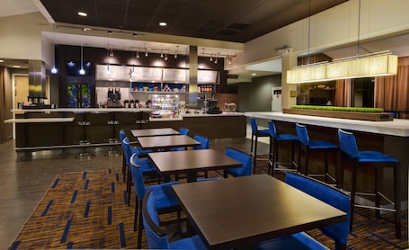 A modern restaurant with a bar area, seating with blue chairs, and a patterned carpet.