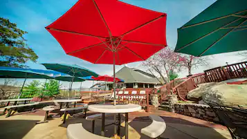 An outdoor patio with round tables and benches, surrounded by red and green umbrellas.