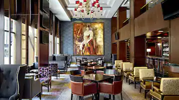 A spacious lobby with a large chandelier, a bar area, and a seating arrangement with multiple tables and chairs.