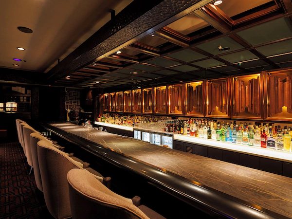 A bar area with a long counter, multiple seating options, and a variety of bottles and glasses.