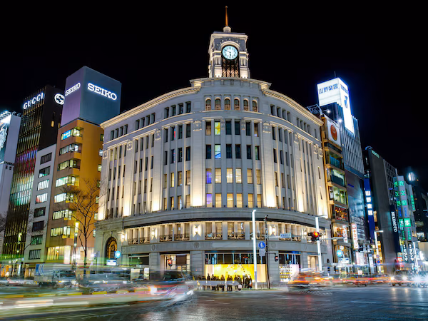 A historic building with a clock tower, surrounded by modern high-rise buildings with illuminated signage.