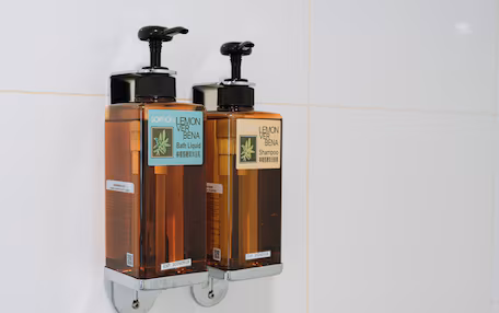 Two wall-mounted dispensers, one for bath liquid and one for shampoo, with labels and QR codes.