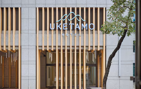 The exterior of the Uketamo Hotel with a modern design, featuring a prominent sign and a tree in front.