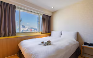 A hotel room with a large bed, a window with curtains, a wooden headboard, and a bedside table with a lamp.