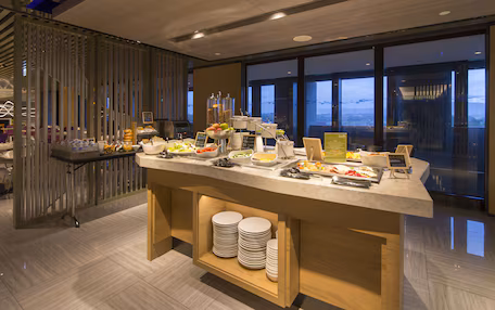 A buffet setup with various food items and a view of the cityscape through large windows.