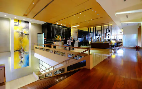 A spacious lobby with a wooden floor, a staircase, and a large abstract painting on the wall.