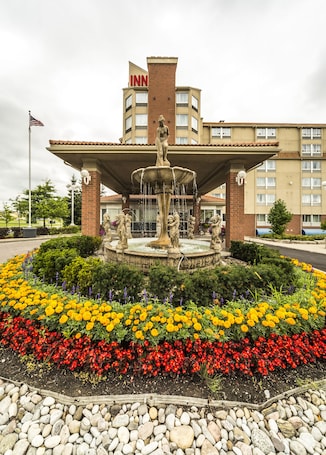 A hotel with a central fountain, surrounded by a flower bed with marigolds and red flowers, and a brick facade.