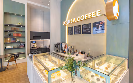 A coffee shop interior with a glass display case of pastries, a coffee machine, and a menu board.