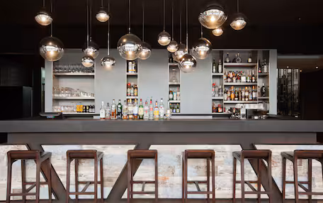 A bar area with multiple stools, shelves stocked with bottles, and hanging spherical light fixtures.