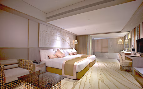 A modern hotel room with a large bed, a sitting area with a glass coffee table, and a separate desk with a chair.