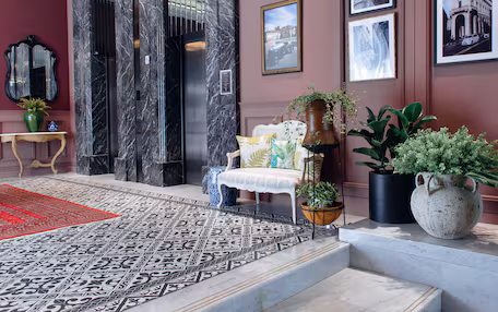 A lobby with a marble floor, a white sofa, a red rug, a mirror, and framed pictures on the wall.