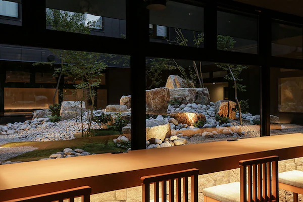 A modern interior with a long wooden table and chairs, large windows, and a rock garden view.