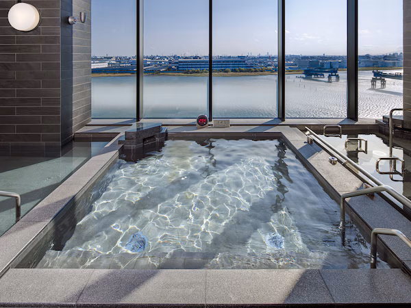 A hot tub with a view of a river and industrial buildings.