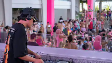 A DJ booth with a Pioneer DJ controller, a crowd in the background, and a pink column.