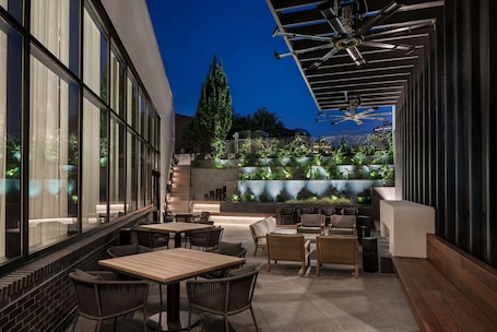 An outdoor seating area with tables and chairs, a water feature, and a staircase leading to an upper level.