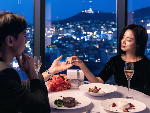 A couple dining at a table with a city view at night.