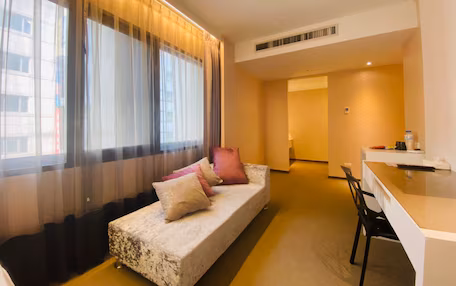 A modern hotel room with a sofa, a dining area, and a view of the city.