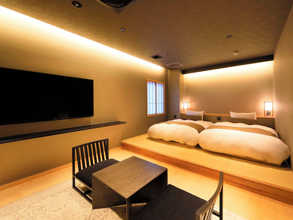 A modern hotel room with a large bed, a flat-screen TV mounted on the wall, a small table, and a seating area.
