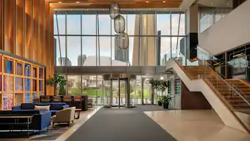 A spacious lobby with a central seating area, a staircase, and large windows offering views of the cityscape.