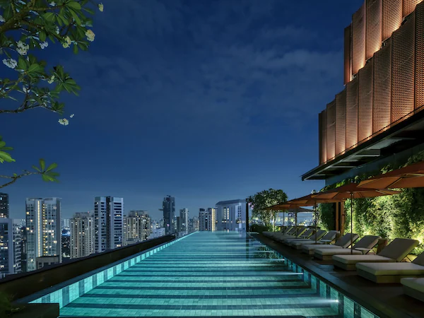 A rooftop infinity pool with lounge chairs and a city view at dusk.