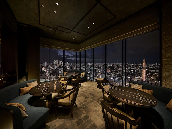 A modern lounge with a city view, featuring a sofa, tables, and chairs.