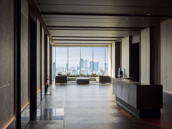 A modern hotel lobby with a long corridor, a reception desk, and a seating area with a city view.