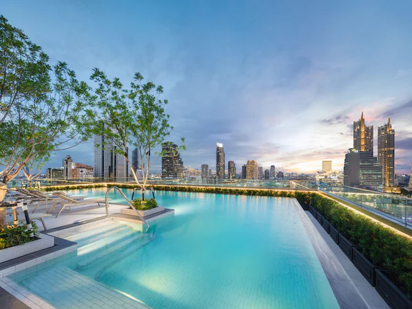 A rooftop infinity pool with a city skyline view, surrounded by trees and modern buildings.