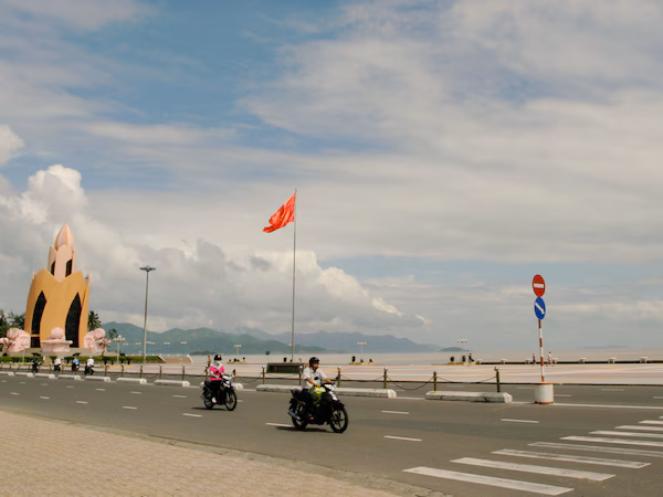 A road with traffic signs, a large lotus-shaped monument, and a flagpole with a flag.