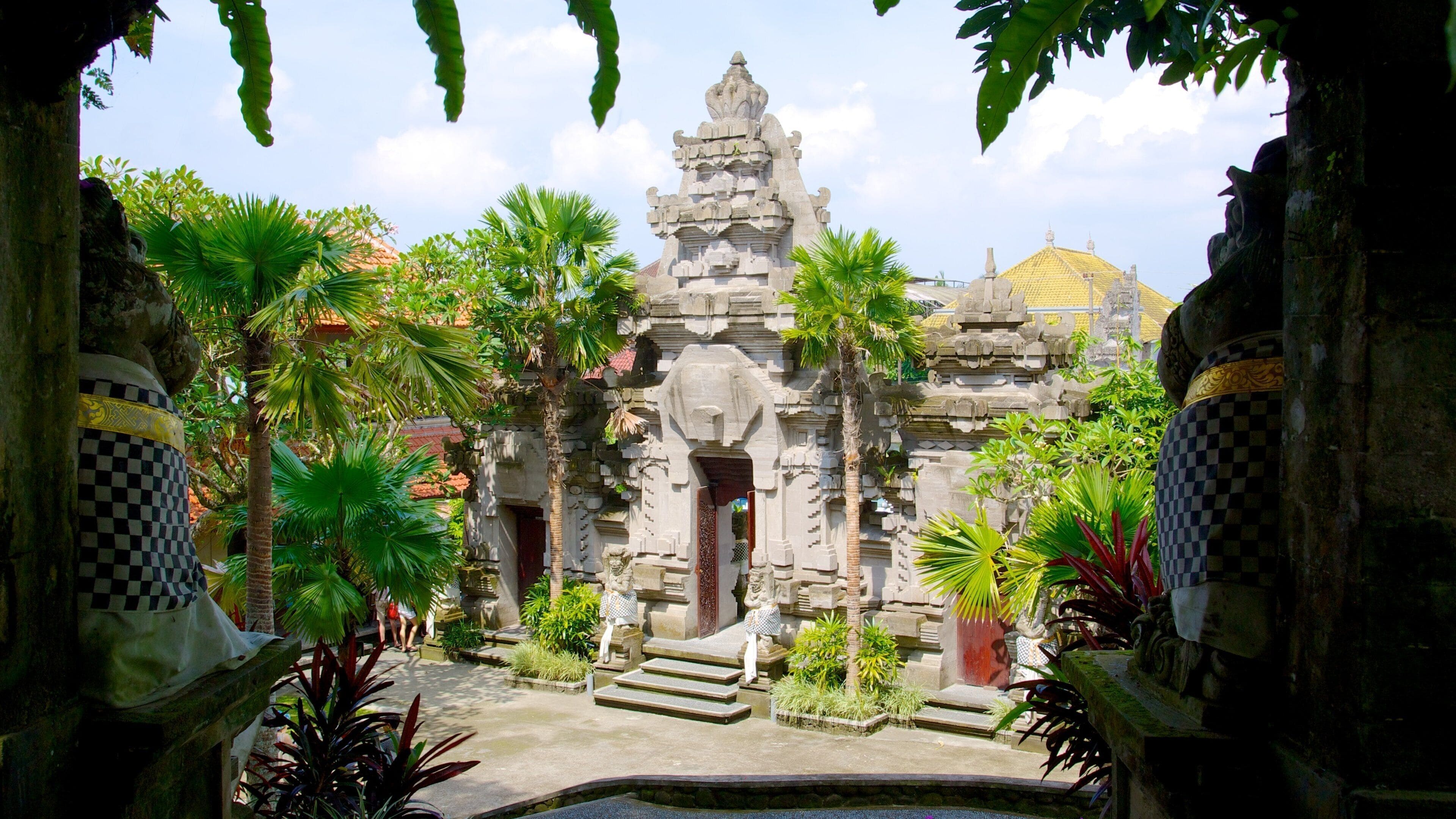 A temple with intricate carvings, surrounded by lush greenery and palm trees.